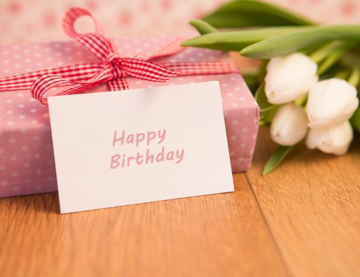 A birthday card, wrapped gift, and white tulips on a table.