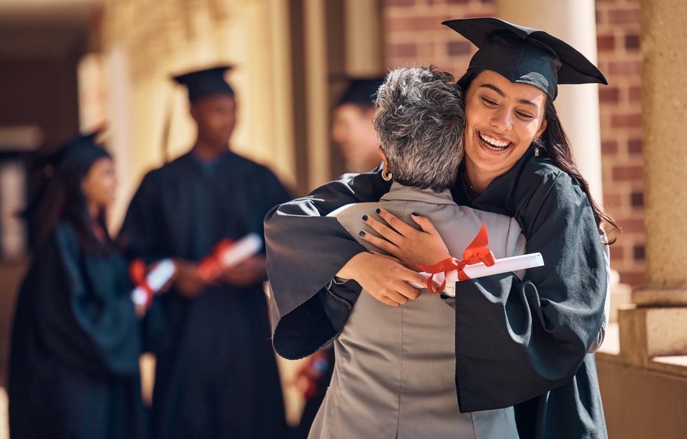Young woman graduate in cap and gown hugging older woman